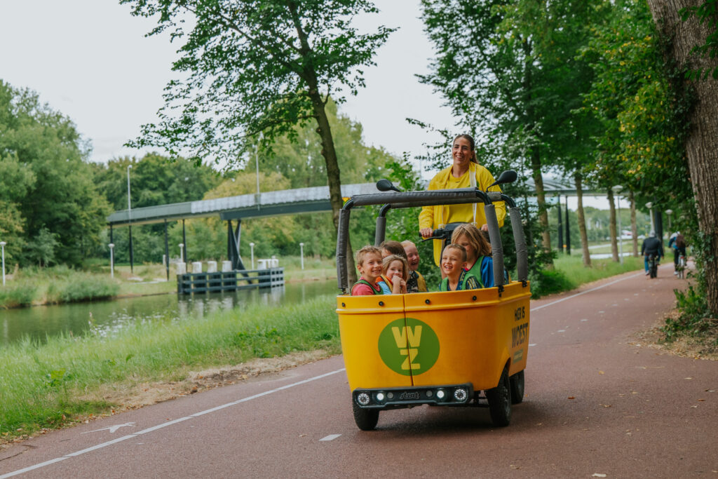 Begeleidster van Woest Zuid rijdt kinderen rond in de gele Woest-bakfiets tijdens de recruitmentcampagne